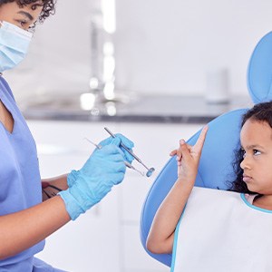 Little girl in dental chair looking unhappy pointing up