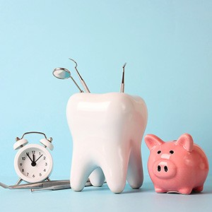 Large model tooth with dental instruments next to alarm clock and piggy bank